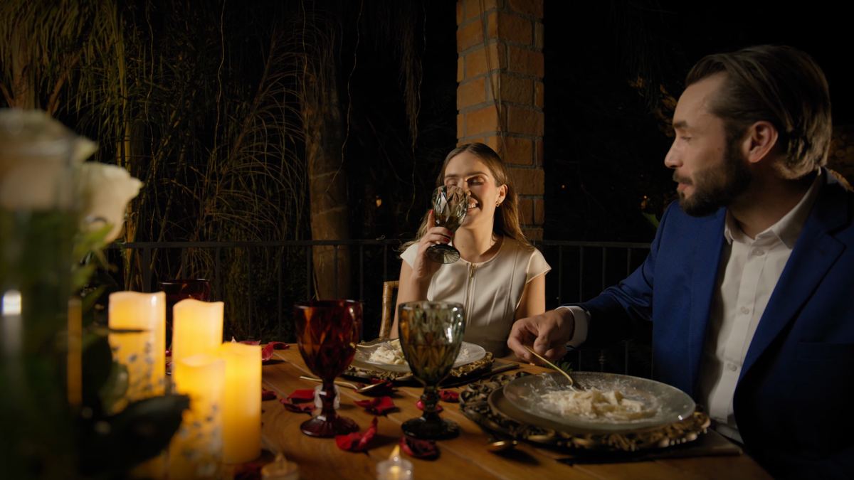 A couple dining by candlelight at a table set for two, white flowers in the foreground.