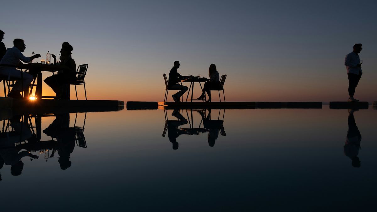 Two tables by the water at dusk, guests in silhouette.