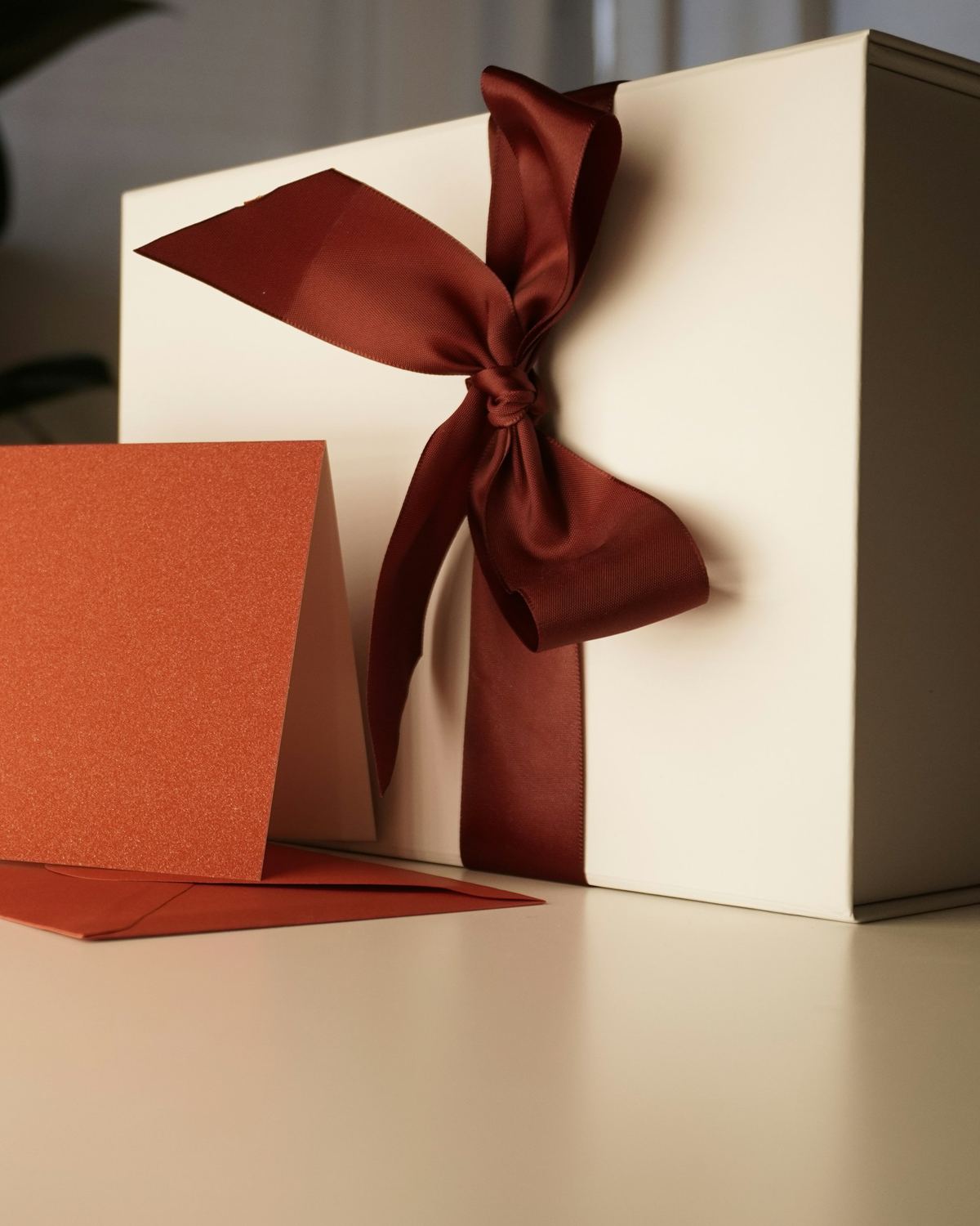 A cream gift box tied with a deep red silk ribbon, a card beside it.