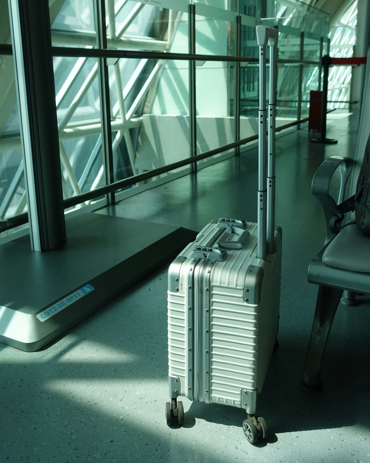 An aluminium suitcase waiting by the glass wall of an airport terminal.
